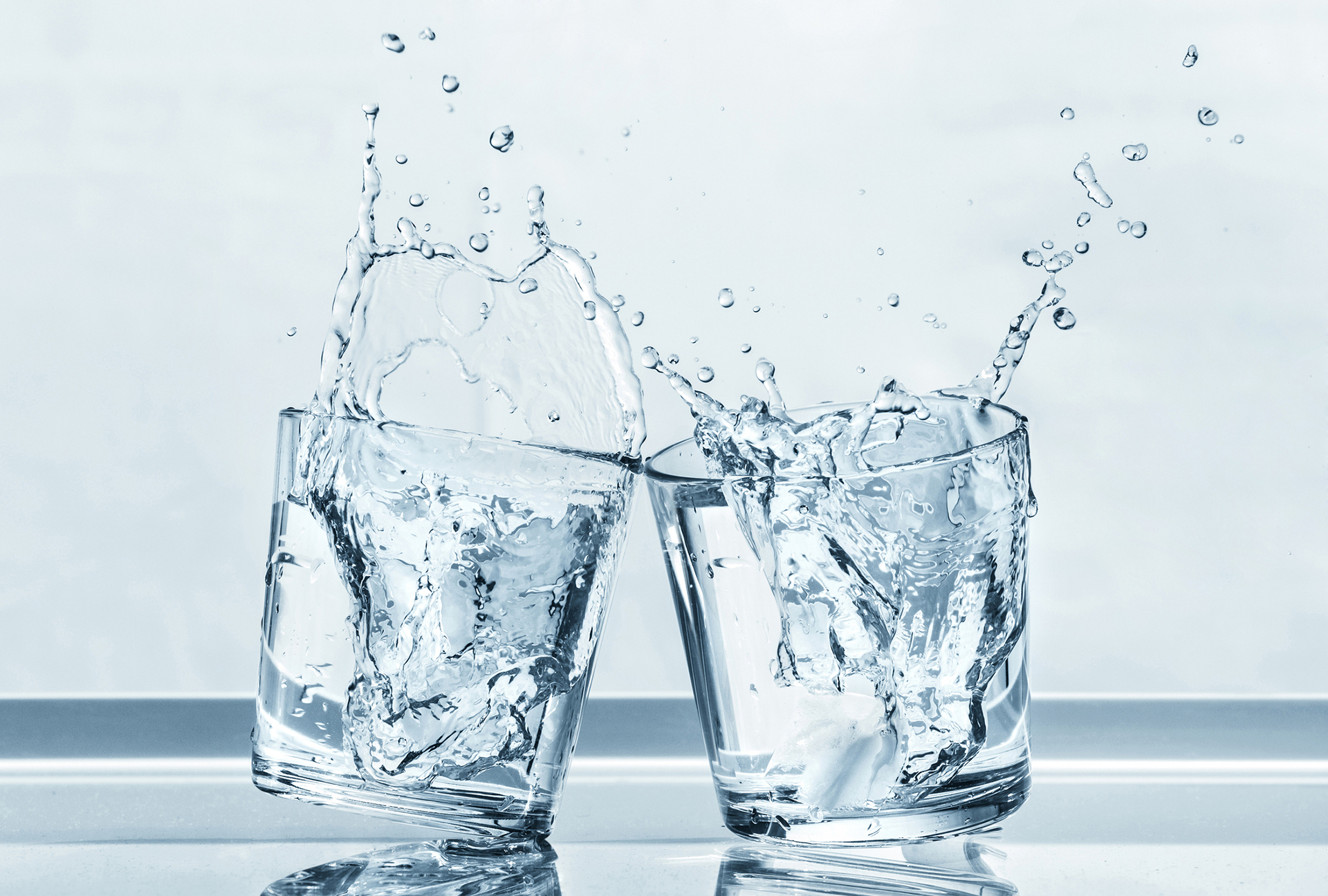 Two glasses of water clinking together with droplets splashing out